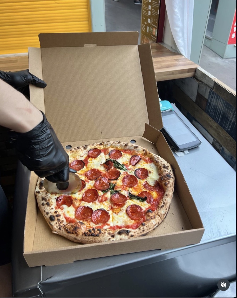 Fresh pepperoni pizza being sliced in its box at the stall